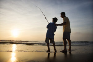 Father,And,Son,Fishing,In,Ocean,Surf,At,Sunset.
